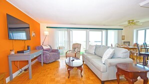 A living room with a sofa, armchairs, a coffee table, a TV, and a dining area with chairs and a table.