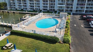 A swimming pool surrounded by lounge chairs and umbrellas, with a parking lot and a building in the background.
