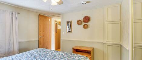 Un dormitorio con cama, ventilador de techo, puerta de madera, mesita de noche de madera y una pared decorada con placas.