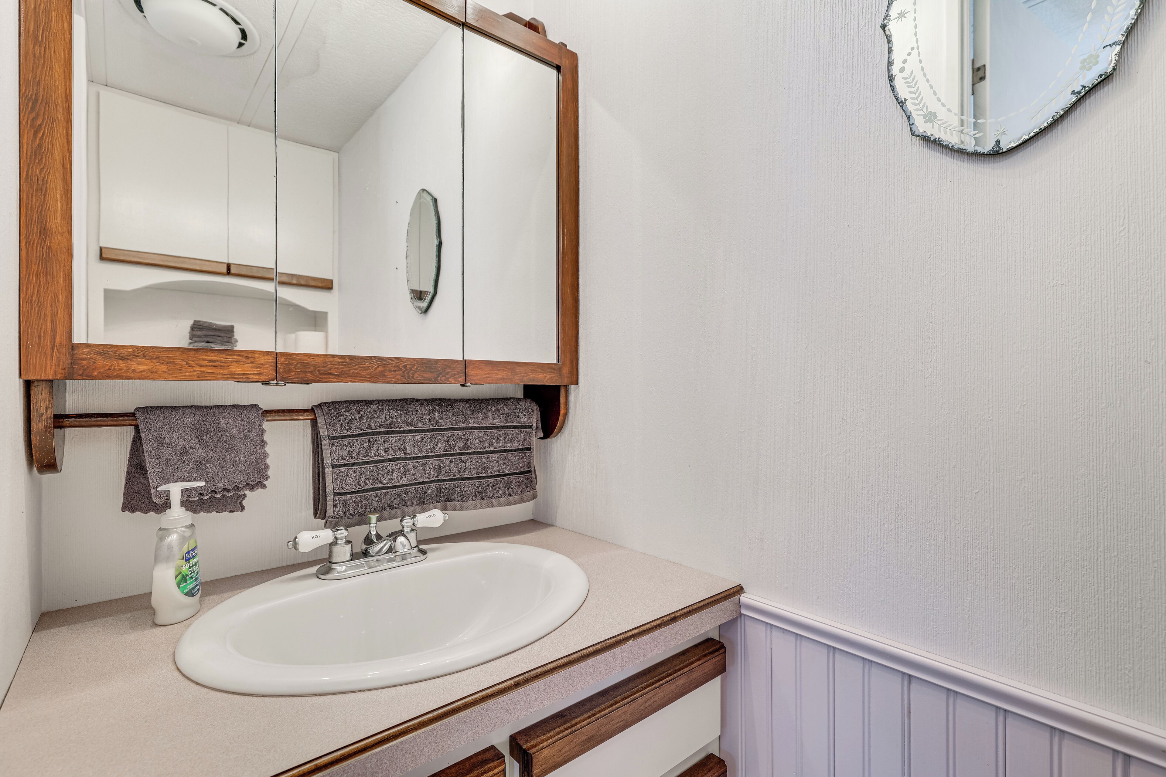 Une salle de bain avec un lavabo blanc, un meuble-lavabo en bois, un grand miroir et un porte-serviettes.