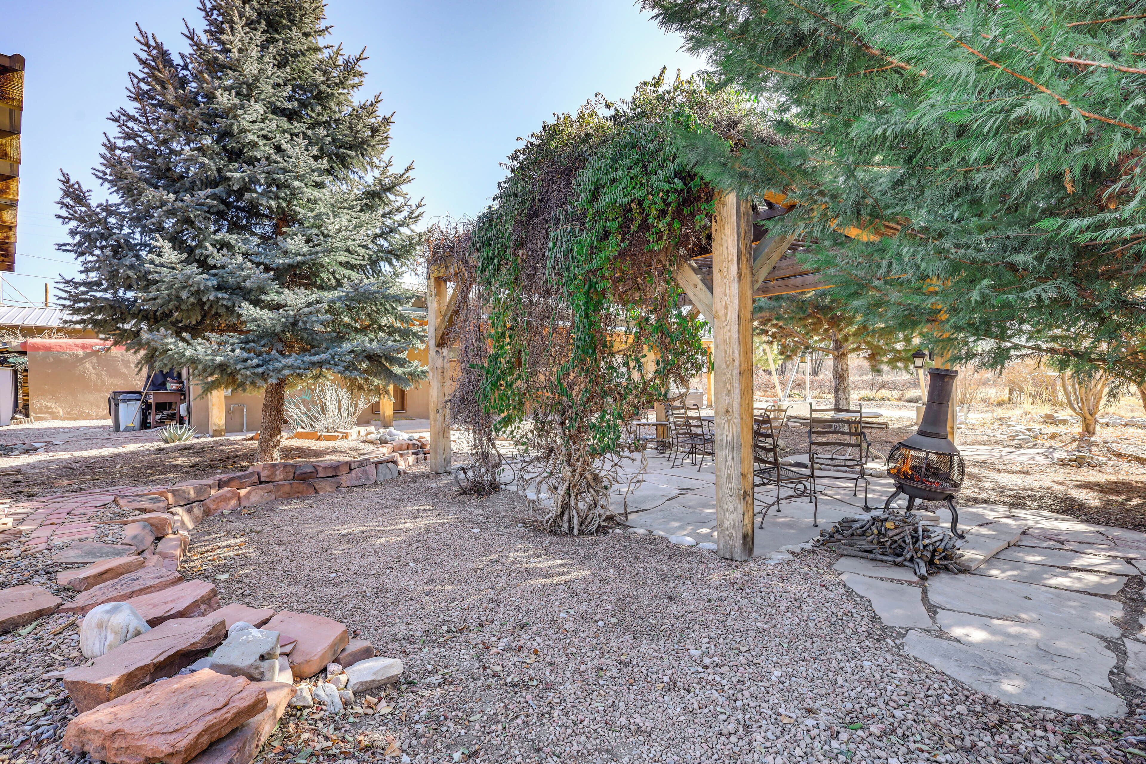 Un patio con una chimenea de piedra, una pérgola de madera y un gran árbol de hoja perenne.
