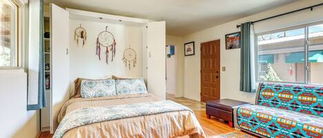 A bedroom with a bed, a sofa, a patterned rug, and a window with curtains.