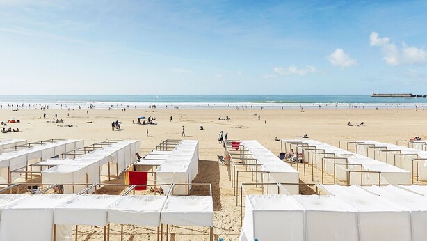 Ein Strand mit Reihen weißer Zelte und einem klaren Himmel.