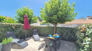 Eine Terrasse im Freien mit Tisch, Stühlen und einem roten Sonnenschirm, außerdem ein Baum.