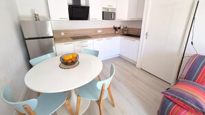 Eine moderne Küche mit weißen Schränken, einer schwarzen Mikrowelle und einem Edelstahlkühlschrank. Ein runder Tisch mit Stühlen und eine Schüssel mit Obst sind ebenfalls vorhanden.