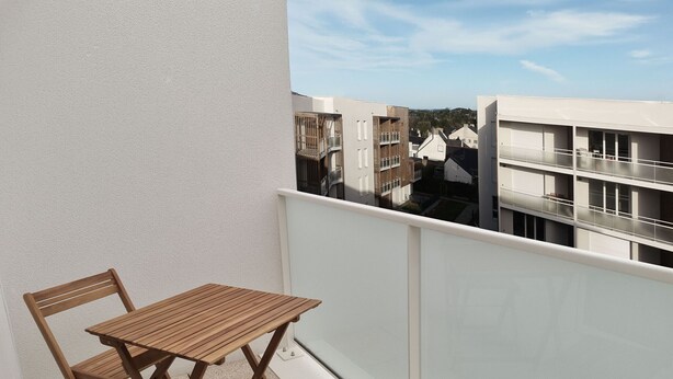 Un balcón con mesa y sillas de madera, con vistas a una zona residencial con edificios modernos.