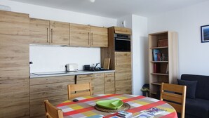 Una cocina compacta con armarios de madera, horno integrado y un comedor con una mesa lista para dos.