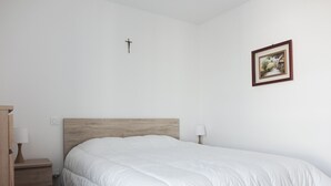 Un dormitorio con cabecera de madera, cubrecama blanco, mesita de noche con lámpara y un cuadro enmarcado en la pared.