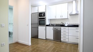 Una cocina moderna con armarios blancos, electrodomésticos de acero inoxidable y piso de madera en patrón de espiga.