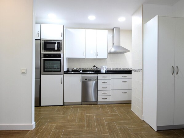 Una cocina moderna con armarios blancos, electrodomésticos de acero inoxidable y un piso con diseño en espiga.