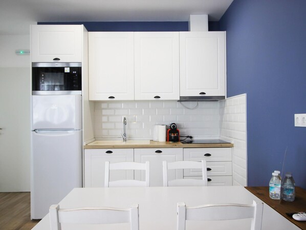 A compact kitchen with white cabinets, a built-in microwave, a sink, and a table with chairs.