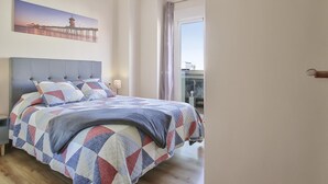 Un dormitorio con una cama grande, cabecera, lámpara colgante, mesita de noche, una lámpara, ventana con cortinas y un cuadro en la pared.