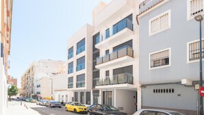 Un edificio moderno con varios pisos, balcones y un estacionamiento con varios autos.