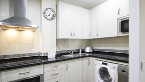 A modern kitchen with white cabinets, a stainless steel range hood, a microwave, a washing machine, and a clock on the wall. - Renovated 1-bedroom apartment near the beach with parking & air conditioning in Málaga (Málaga)