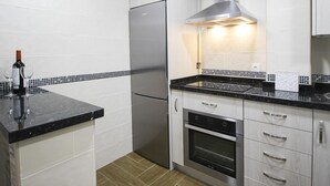 A modern kitchen with a stainless steel refrigerator, a built-in oven, and a microwave. There is a clock on the wall and a wine bottle on the counter. - Renovated 1-bedroom apartment near the beach with parking & air conditioning in Málaga (Málaga)