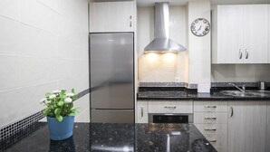 A modern kitchen with white cabinets, a stainless steel refrigerator, a black countertop, and a clock on the wall. - Renovated 1-bedroom apartment near the beach with parking & air conditioning in Málaga (Málaga)
