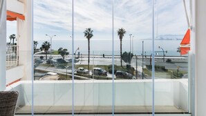 Un balcón con vista a una carretera costera, palmeras y un barco a lo lejos.