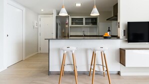 Una cocina moderna con una isla central, dos taburetes de bar, luces colgantes, un refrigerador, un microondas y un televisor de pantalla plana.
