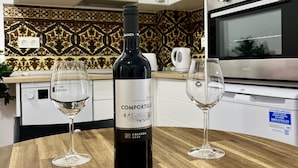 A bottle of Crianza 2020 wine on a wooden table with two empty wine glasses.
