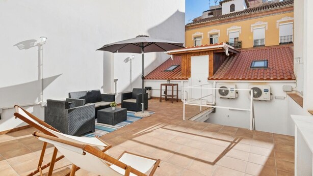 A rooftop terrace with outdoor seating, a hammock, and a view of adjacent buildings.