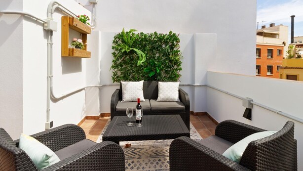 Un balcón con muebles de mimbre, una pared cubierta de plantas verdes y una botella de vino.