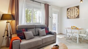 Una sala de estar con un sofá gris, una pequeña mesa de centro de madera, una lámpara y un comedor con una mesa y sillas.