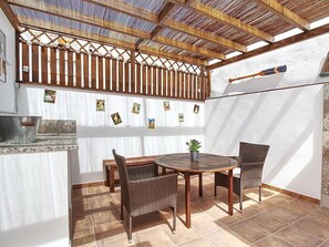 Une terrasse avec une table ronde en bois et des chaises en osier, un plafond en bambou et un mur blanc orné de petites images.