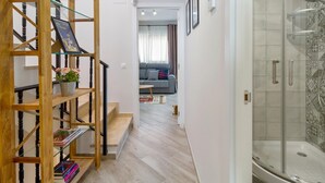 Una escalera con estructura de madera y estantes de vidrio, que lleva a una sala de estar con sofá y cabina de ducha de cristal.