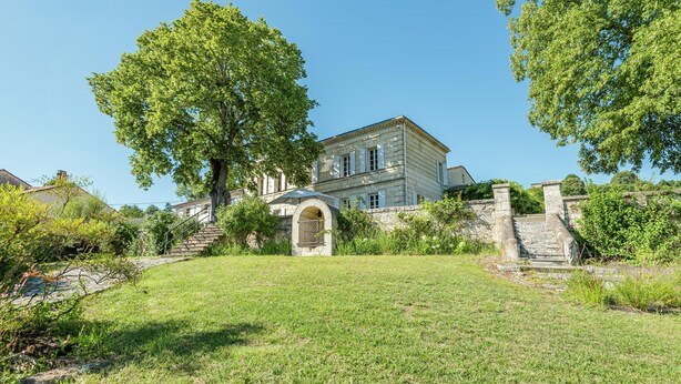 A large, historic building with a prominent arched entrance, surrounded by lush greenery and a well-maintained lawn. - Beautiful Stone House near Saint-Émilion and Libourne (Saint-Germain-de-la-Rivière)