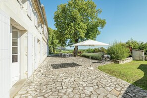 A stone-paved courtyard with outdoor seating, a large tree, and a barbecue grill.