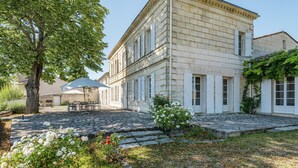 A historic building with a stone facade, a paved courtyard, and a tree providing shade. - Beautiful Stone House near Saint-Émilion and Libourne (Saint-Germain-de-la-Rivière)