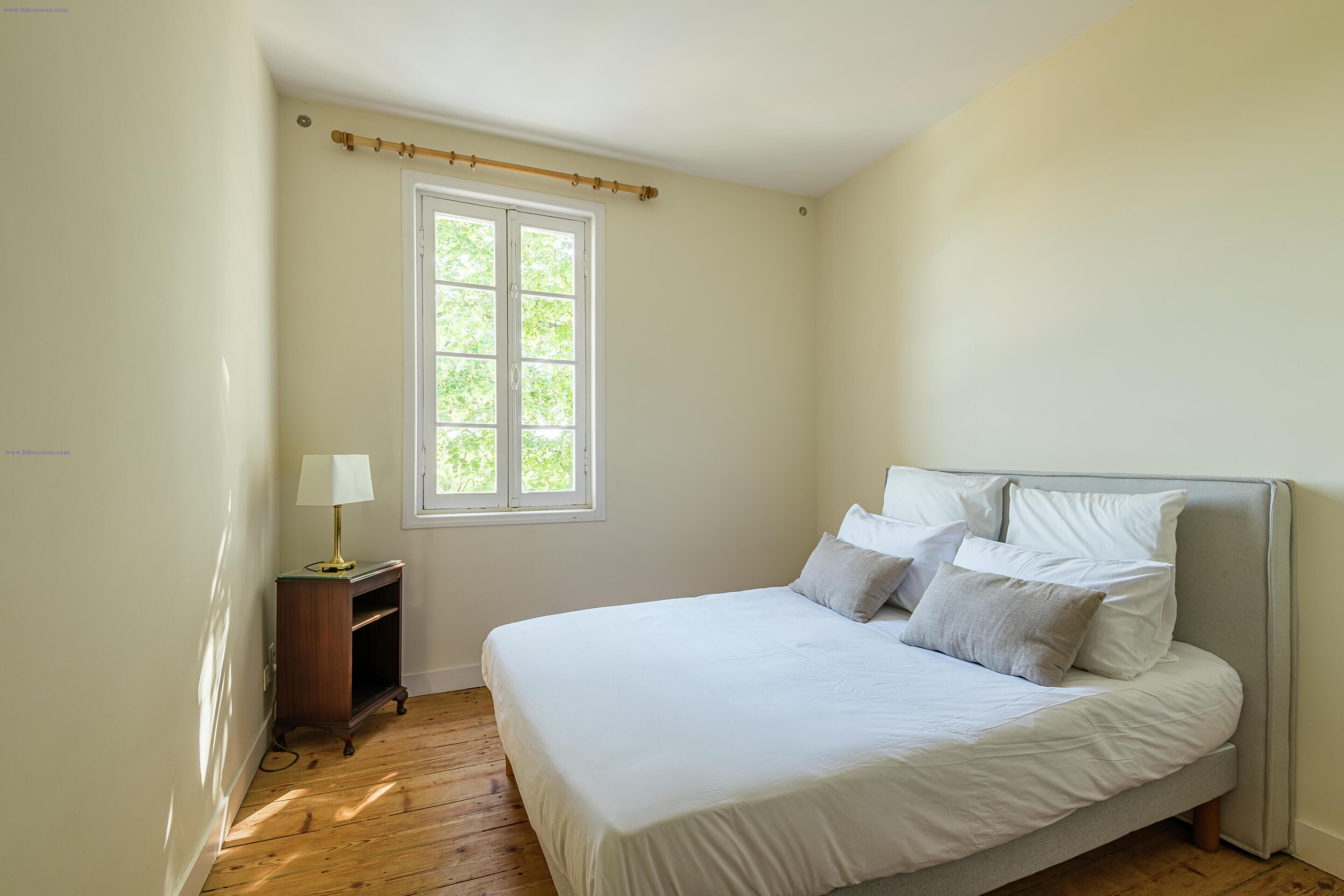 Une chambre à coucher avec un lit, une table de chevet avec une lampe, une fenêtre et un plancher en bois.