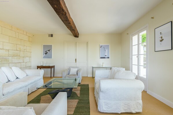 A spacious living room with white furniture, a glass coffee table, and a large window.