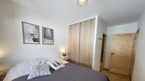 Un dormitorio con una cama, dos cuadros enmarcados, una mesita de noche, un armario de madera y una puerta.