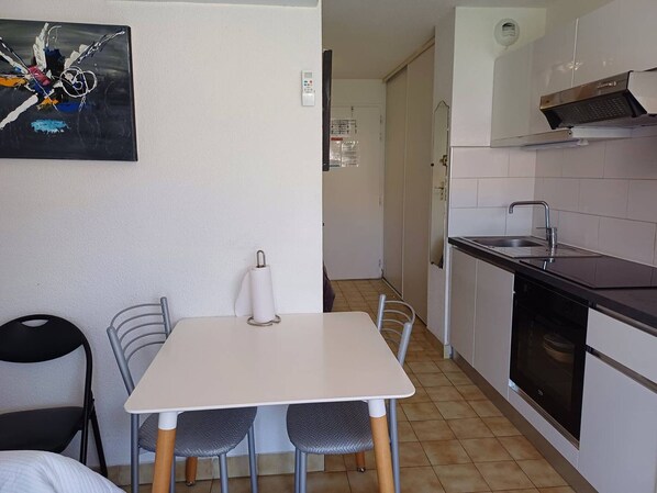 Una cocina compacta con una mesa y sillas blancas, un lavamanos y una estufa.