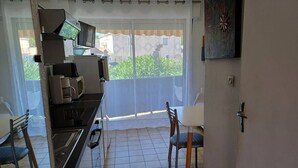 A compact kitchen with a microwave, coffee maker, and stove. There is a dining area with a table and chairs, and a balcony with a view of greenery.