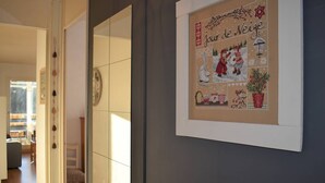 A hallway with a framed artwork depicting a winter scene, a mirror, and a door leading to another room. - Cozy 2-Room Apartment in Bolquère, Near Shops and Skiing (Bolquère-Superbolquère)