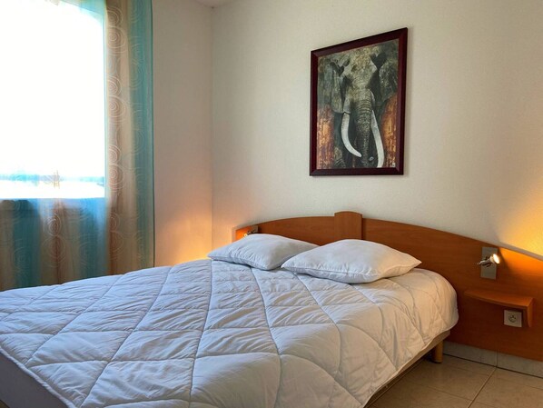 A neatly made bed with a quilted white duvet, a wooden headboard, and a framed picture of an elephant on the wall.