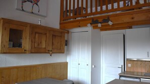 A room with wooden cabinets, a bench, a table, and a loft area with a railing. - Cozy 2-room apartment with garden in Bolquère (Bolquère-Pyrénées 2000)