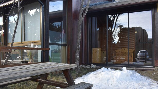 A wooden picnic table outside a building with large windows and a garage door visible in the background. - Cozy 2-room apartment with garden in Bolquère (Bolquère-Pyrénées 2000)