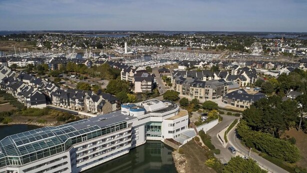 Un hôtel situé au bord de l’eau, avec plusieurs étages, une façade en verre et un quai.