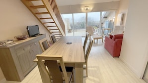 Une cuisine moderne avec une table et des chaises en bois, un téléviseur encastré et un escalier menant à un balcon.