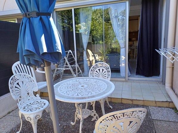 Une terrasse dotée de mobilier en métal blanc, comprenant une table et des chaises, ainsi qu’un parasol bleu.