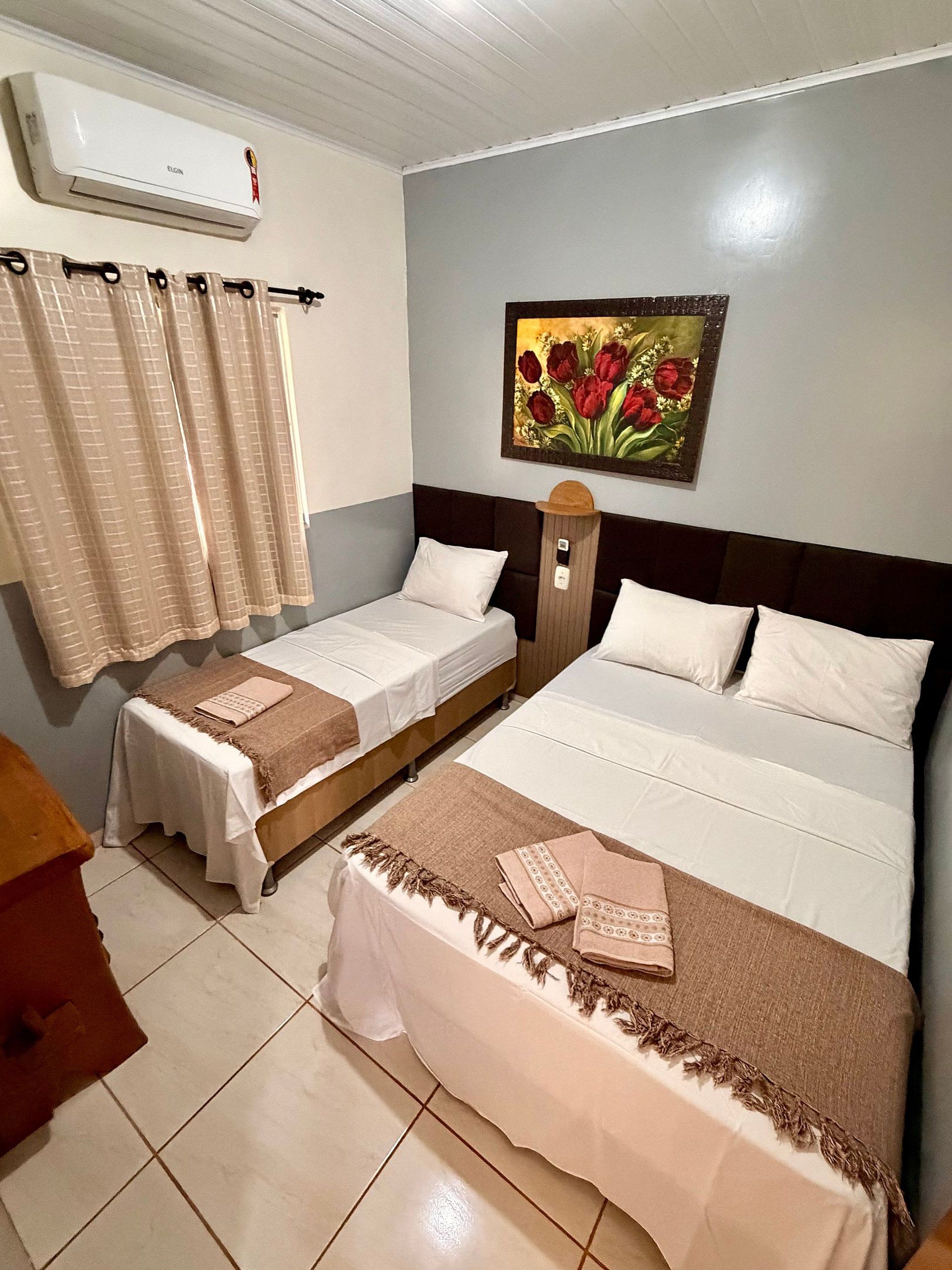 A hotel room with two beds, a painting of flowers on the wall, and an air conditioning unit.