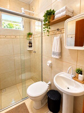 A modern bathroom with a glass shower enclosure, a toilet, a sink, and a mirror. - Casa Flor do Ipê Homes (Nobres)