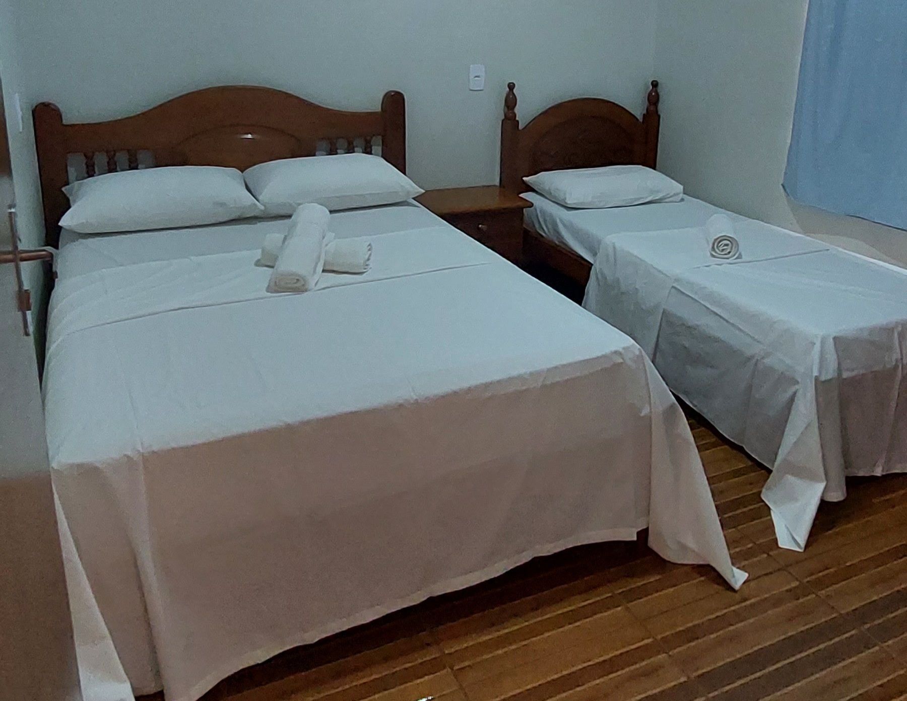 A hotel room with two single beds, each with a wooden headboard, white linens, and a neatly rolled towel.