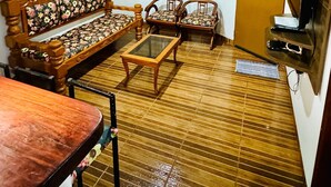 A living room with a wooden floor, a sofa, two chairs, a coffee table, a ceiling fan, a painting, a window with curtains, and a door. - Casa Flor do Ipê Homes (Nobres)