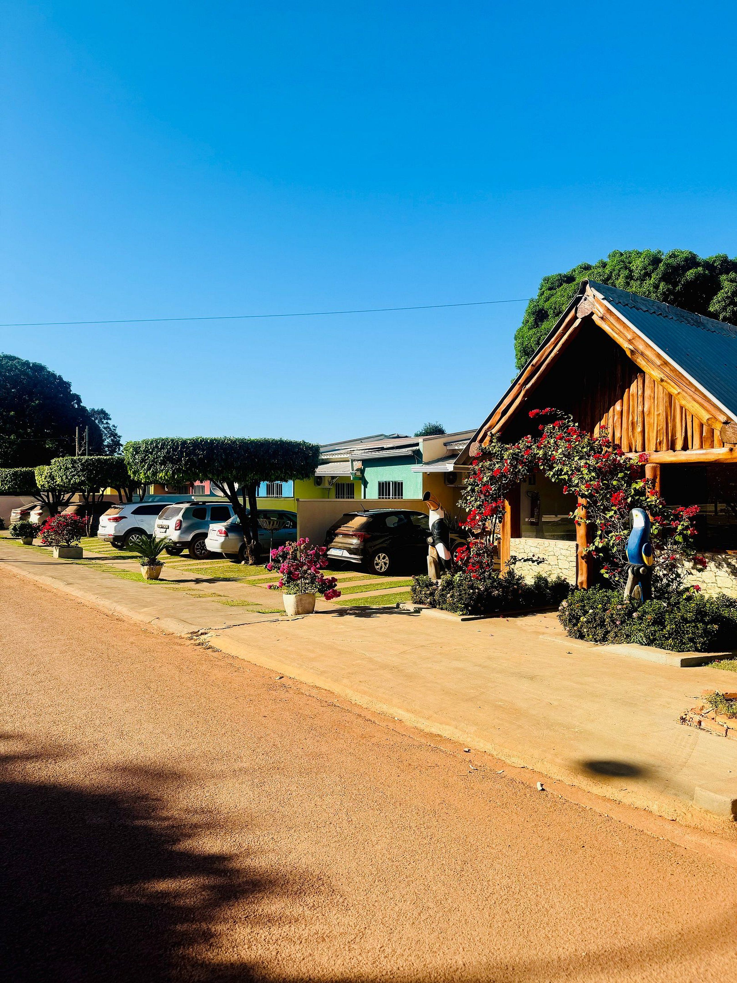 A rustic building with a sloped roof, surrounded by parked cars and potted plants.