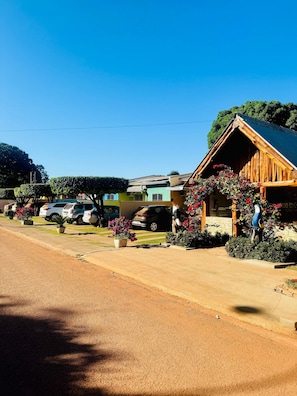 A rustic building with a sloped roof, surrounded by parked cars and potted plants. - Casa Flor do Ipê Homes (Nobres)