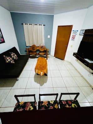 A living room with a sofa, a wooden bench, a small table, and a television. - Casa Flor do Ipê Homes (Nobres)